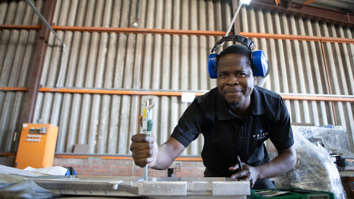 Man wearing ear dampeners inspecting die cast alloy part with micrometer.