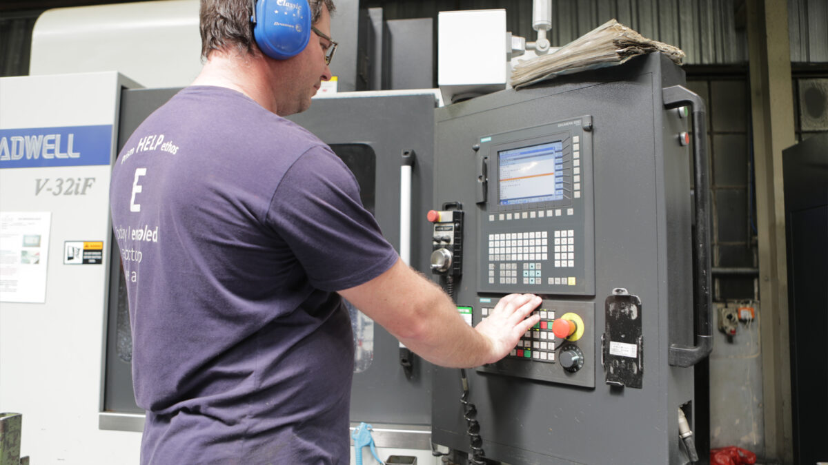 Man with glasses wearing ear dampeners checking gauges at manufacturing facility.