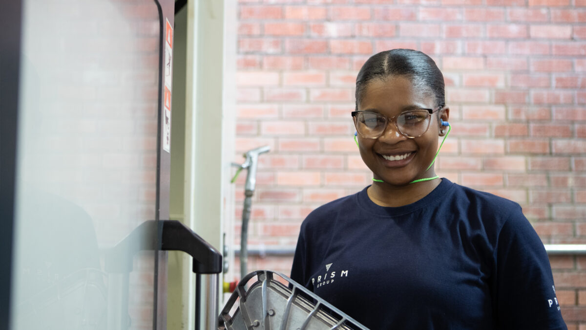 Woman wearing safety glasses holding alloy die cast part and smiling.