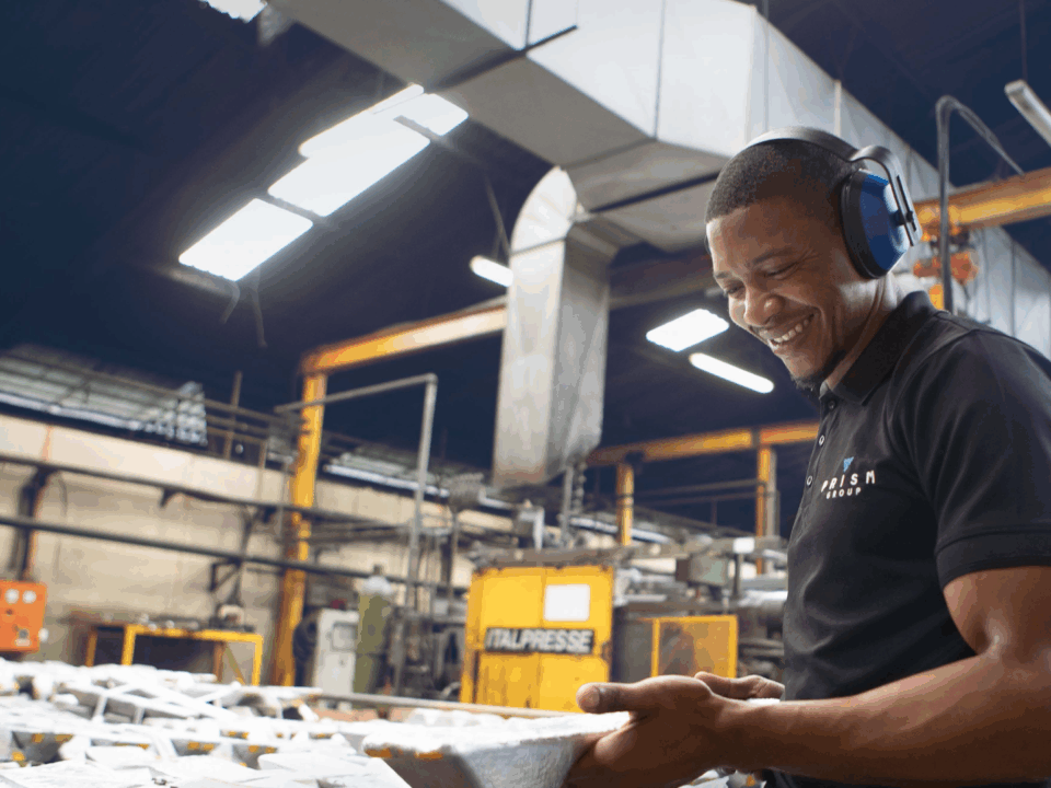Young man holding a Die Cast part in a Prism manufacturing facility.